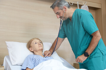 Wall Mural - Doctor or assistance staff talking with an elder patient woman while using stethoscope and sleep on bed in the hospital