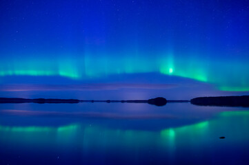 northern lights dancing over calm lake in farnebofjarden national park in north of sweden.