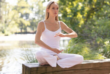 A Slim Woman In White Clothing Doing Tai Chi Outside