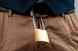 Close-up of a gold padlock hanging from a man's belt. The concept of marital fidelity, celibacy, treason, chastity belt.