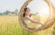 © kwanchaichaiudom - Happy girl sits in wicker swing among the golden rice fields.