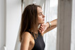 © Volodymyr - Portrait of young pensive caucasian brunette woman posing in black underwear and blue jeans, standing behind a open window in white studio. Model tests of pretty girl in basic clothes.