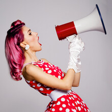 Beauty Red Haired Woman Holding Megaphone, Shout. Girl In Pin Up Style Dress, Over Grey Background. Pinup Model Posing In Retro Fashion Vintage Studio Concept Image. Square.