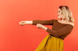 © khosrork - Side view portrait of strong ambitious woman in brown blouse pretending to pull invisible rope, concept of hard work, striving and efforts to achievement. Indoor studio shot isolated on red background