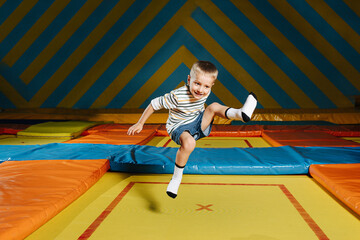 Enthusiastic little boy jumping on a square trampoline in entertainment center. Hovering in an awkward position.