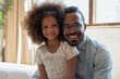 Daddy and his princess. Family portrait of single african father and lovely little daughter schoolgirl posing in living room, happy black foster dad and adopted child hugging smiling looking at camera