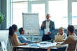 © Kostiantyn - Confident mature businessman giving a presentation, explaining something to colleagues while having a meeting in the office