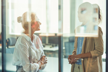 Two diverse female coworkers having informal conversation while standing in the modern office