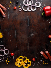 Space For Text, Frame Made From Fresh Vegetables, Bulgarian Pepper, Red Onion Rings, Sausages, Herbs. Dark Background