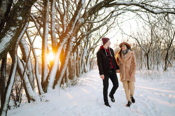 Wall Mural - Young couple on winter holiday in a snowy forest at sunset. Handsome young man embracing his girlfriend in a winter day. People, season, travel, love and leisure concept.