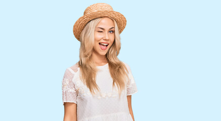 Poster - Young blonde girl wearing summer hat winking looking at the camera with sexy expression, cheerful and happy face.