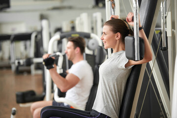 Wall Mural - Pretty woman doing exercise on chest press. Sporty caucasian girl exercising on machine at gym, side view. People, sport, positive emotions concept.