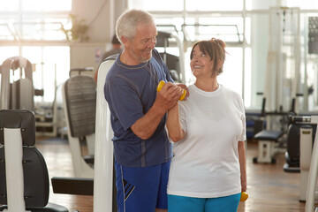 Wall Mural - Happy couple of seniors training at gym together. Smiling elderly couple looking at each other during workout at gym. People, sport, togetherness, relationship concept.