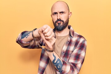 Poster - Young handsome man wearing prisoner handcuffs with angry face, negative sign showing dislike with thumbs down, rejection concept