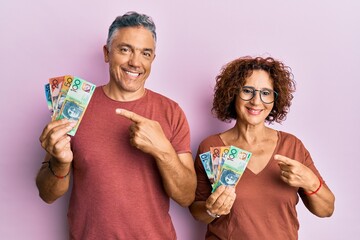 Sticker - Beautiful middle age couple holding australian dollars smiling happy pointing with hand and finger