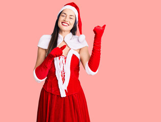 Sticker - Young beautiful caucasian woman wearing santa claus costume pointing to the back behind with hand and thumbs up, smiling confident