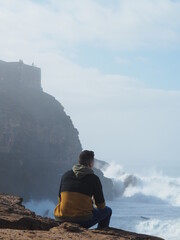 An unrecognizable man in the coast with the rocks and the waves in the background.