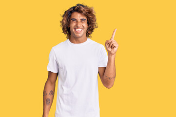 Young hispanic man wearing casual white tshirt with a big smile on face, pointing with hand finger to the side looking at the camera.