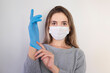 © Hazal - Young woman patient in a medical mask puts on protective surgical sterile gloves on her arm, isolated on gray background, protection against coronovirus See Less