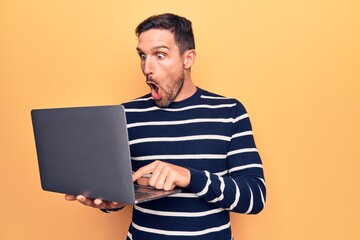 Sticker - Young handsome man working using laptop standing over isolated yellow background scared and amazed with open mouth for surprise, disbelief face