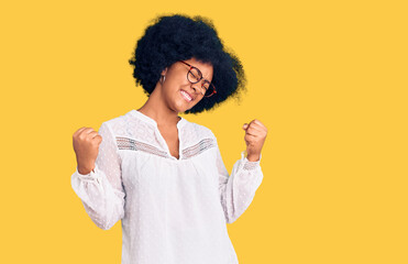 Sticker - Young african american girl wearing casual clothes very happy and excited doing winner gesture with arms raised, smiling and screaming for success. celebration concept.