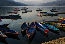 Colorful Boats Floating With No People Anchored On The Phewa Lake, Pokhara, Nepal. Nice Reflection Of The Sky And Clouds On The Water. Large Mountains Far Away On The Background. Post Pandemic Travel