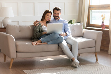 happy young caucasian couple renters relax on sofa in living room watch video on laptop together. sm