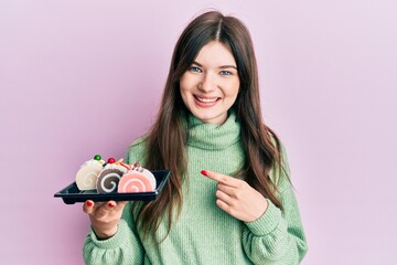 Sticker - Young beautiful caucasian girl holding cake sweets smiling happy pointing with hand and finger