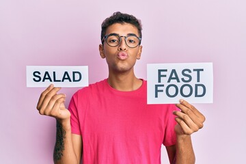 Poster - Young handsome african american man holding salad and fast food message paper looking at the camera blowing a kiss being lovely and sexy. love expression.