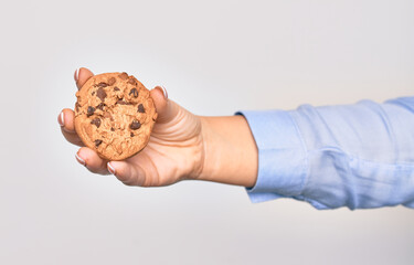 Hand of caucasian young woman holding delicious chocolate cookie over isolated white background