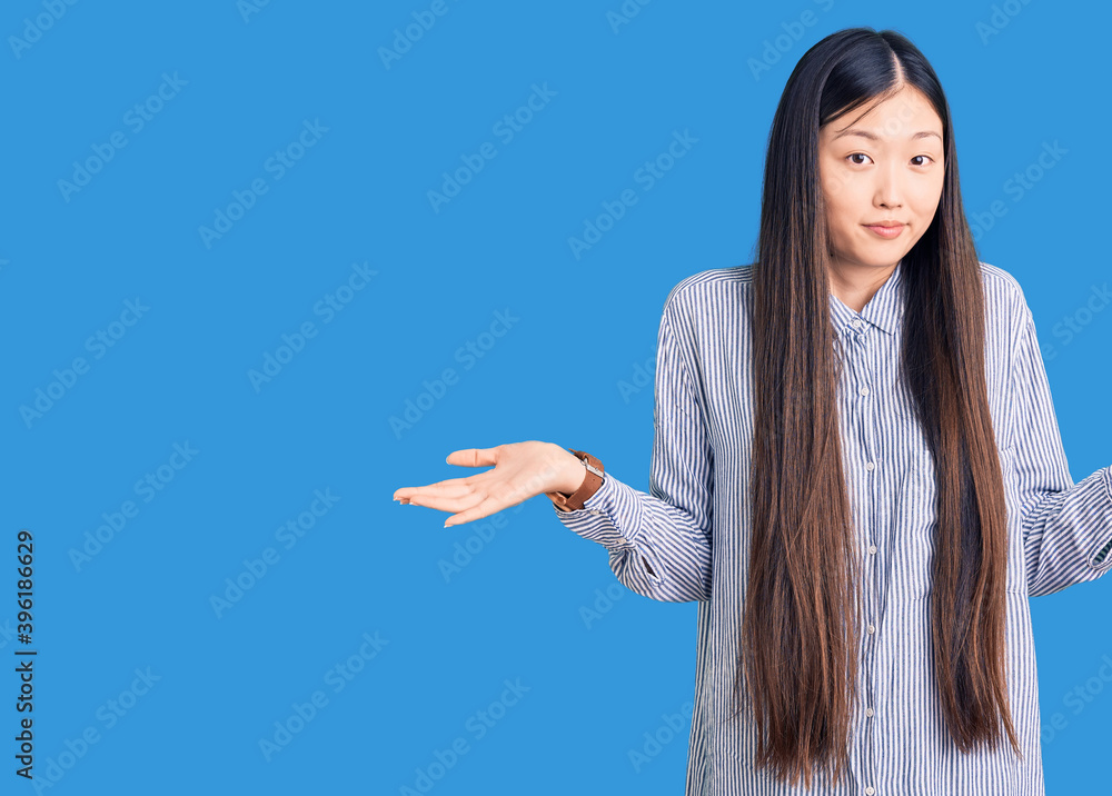 Young beautiful chinese woman wearing casual shirt clueless and confused expression with arms and hands raised. doubt concept.
