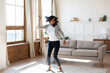 Happy young African American woman tenant relax rest dance alone in cozy light modern living room. Overjoyed smiling millennial biracial female renter have fun enjoy lazy leisure weekend at home.