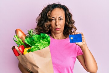 Poster - Middle age hispanic woman holding groceries and credit card depressed and worry for distress, crying angry and afraid. sad expression.