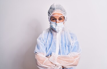 Sticker - Middle age nurse woman wearing protection coronavirus equipment over white background skeptic and nervous, disapproving expression on face with crossed arms. Negative person.