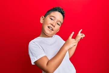 Sticker - Little boy hispanic kid wearing casual white tshirt smiling and looking at the camera pointing with two hands and fingers to the side.