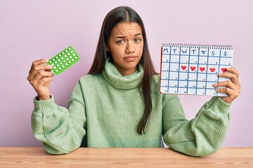 Sticker - Beautiful hispanic woman holding birth control pills skeptic and nervous, frowning upset because of problem. negative person.