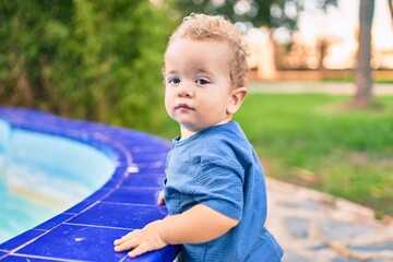 Cute and happy little boy having fun at the park on a sunny day. Beautiful blonde hair male toddler playing outdoors