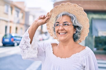 Poster - Middle age woman with grey hair smiling happy wearing summer hat outdoors