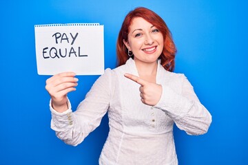 Sticker - Young redhead woman asking for equality economy holding paper with pay equal message smiling happy pointing with hand and finger