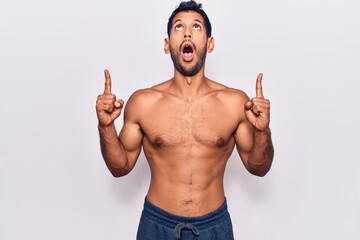 Sticker - Young latin man standing shirtless amazed and surprised looking up and pointing with fingers and raised arms.