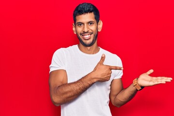 Sticker - Young latin man wearing casual clothes amazed and smiling to the camera while presenting with hand and pointing with finger.