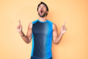 Poster - Handsome hispanic man wearing sportswear amazed and surprised looking up and pointing with fingers and raised arms.