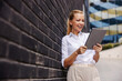 © Dusan Petkovic - Attractive innovative smiling blond fashionable businesswoman standing in front of black wall and using tablet.