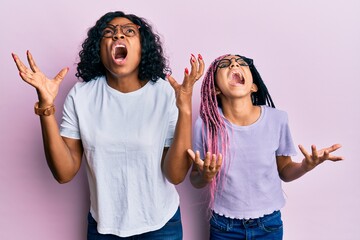 Canvas Print - Beautiful african american mother and daughter wearing casual clothes and glasses crazy and mad shouting and yelling with aggressive expression and arms raised. frustration concept.