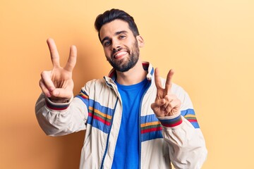 Young handsome man with beard wearing casual jacket smiling looking to the camera showing fingers doing victory sign. number two.