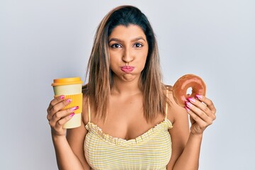 Sticker - Beautiful brunette woman eating doughnut and drinking coffee puffing cheeks with funny face. mouth inflated with air, catching air.