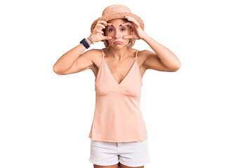 Young blonde woman wearing summer hat trying to open eyes with fingers, sleepy and tired for morning fatigue