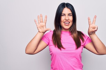 Poster - Young beautiful brunette woman wearing casual pink t-shirt standing over white background showing and pointing up with fingers number seven while smiling confident and happy.