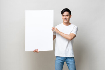 Portrait of handsome Asian man holding empty white placard in isolated studio gray background