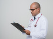 © Chanakon - Physician in white coat, stethoscope writing paper on clipboard by pen look.into note isolated on white background.